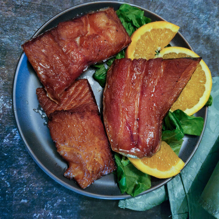 Chunks of smoked steelhead trout garnished with greens and orange wedges.