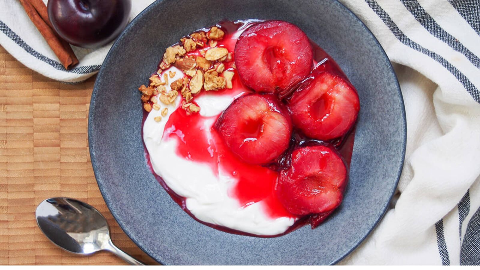 Halved plums in a bowl with yogurt and granola.