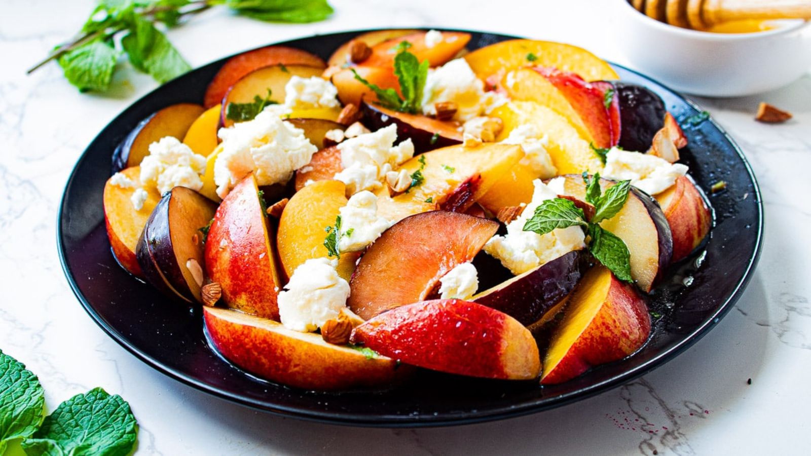 Colorful stone fruit salad with fresh mint leaves and crumbled cheese.