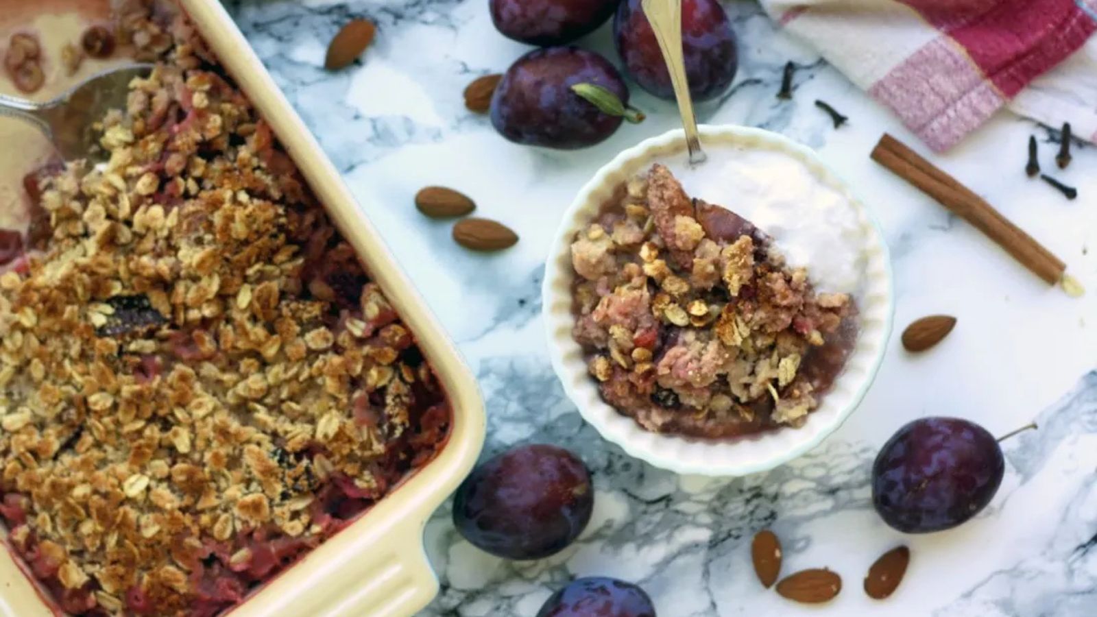 Plum crisp with ice cream in a white bowl with fresh plums.