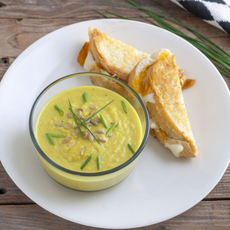 Squash soup in a glass bowl next to a grilled cheese sandwich.