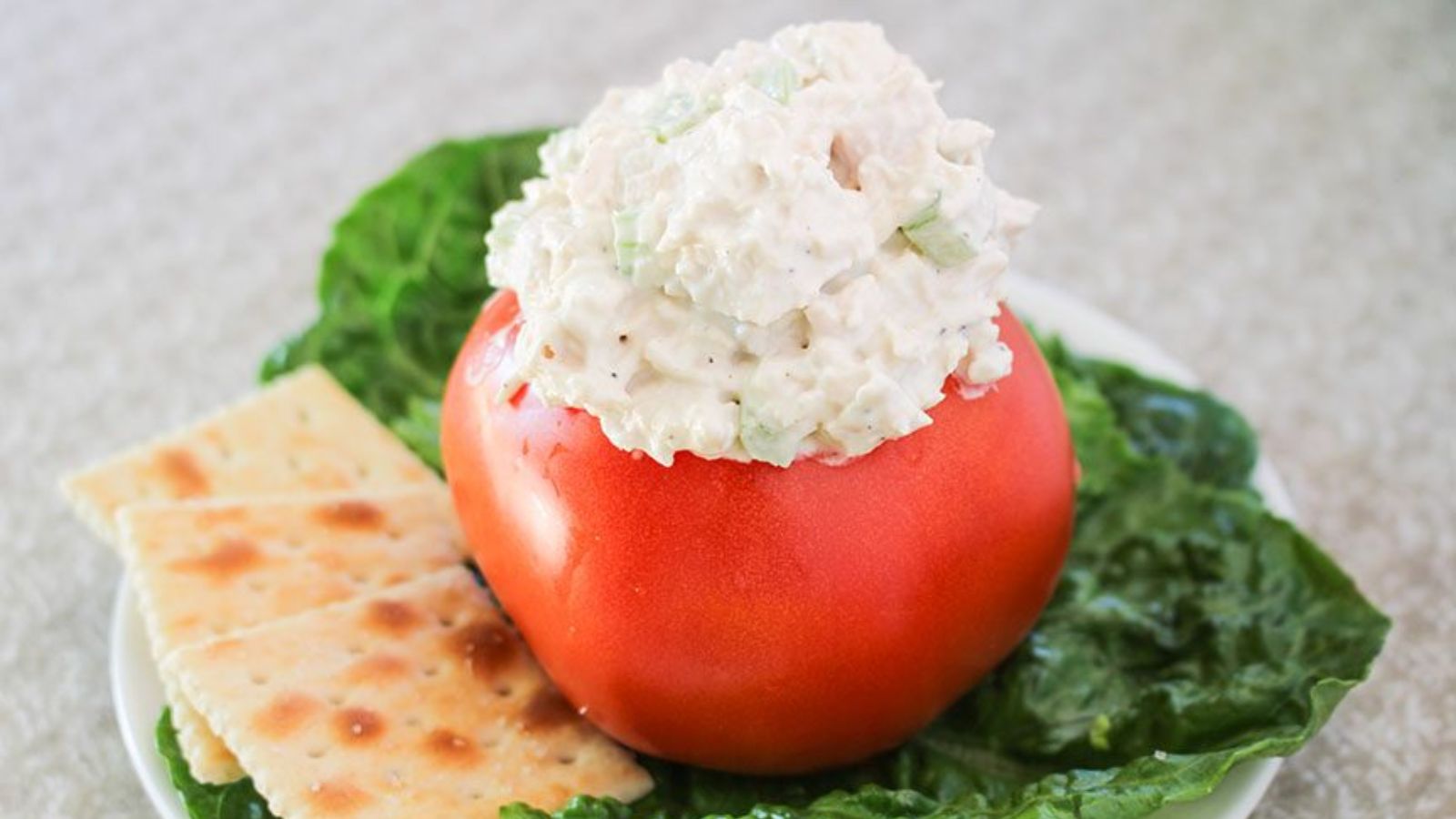 Chicken salad on top of tomato on a plate.