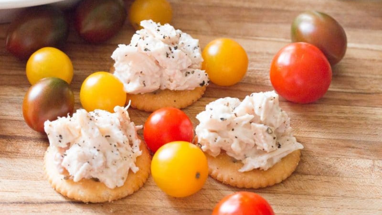 Chicken salad on a bite size bread on a wooden board