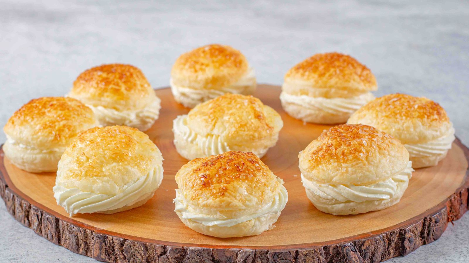 Round cream filled puffs on a wooden slab.