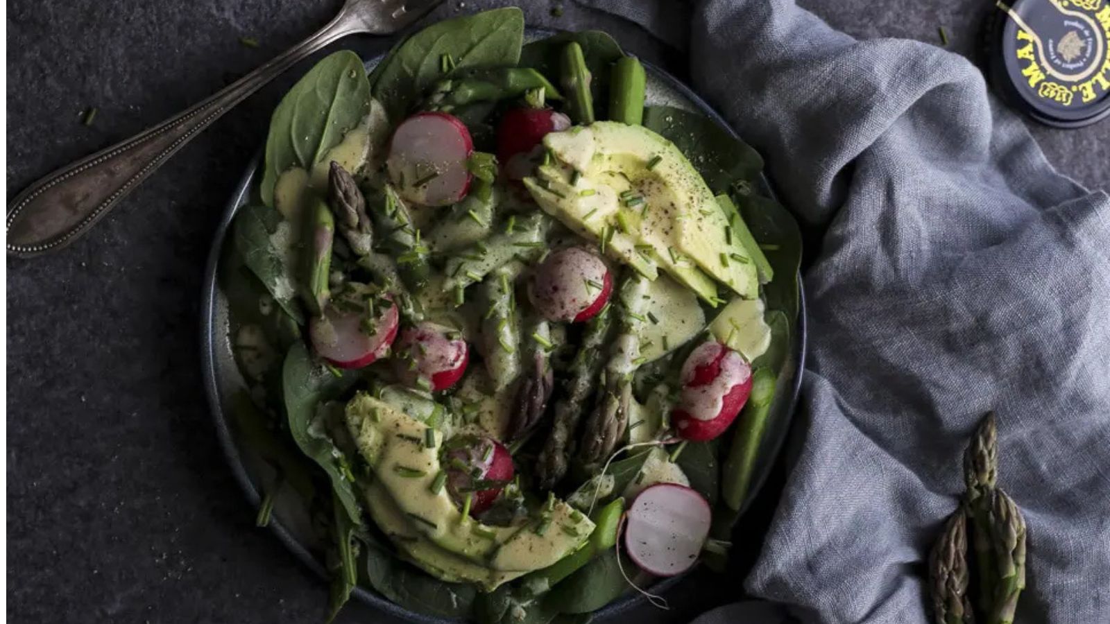 Dark and moody photo of asparagus radish salad on a black plate with a grey towel.