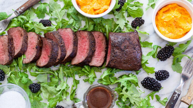 Medium-rare sliced venison loin on a bed of arugula with sides.