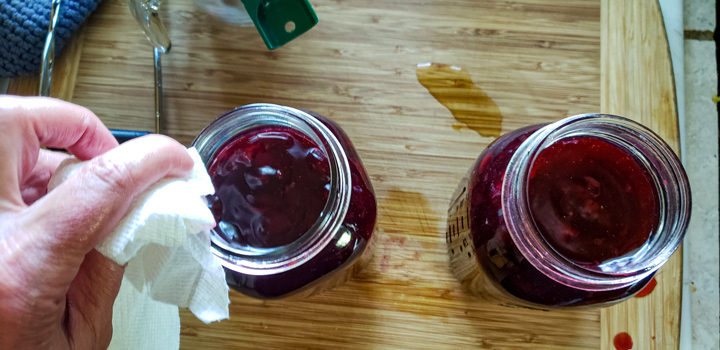 Wiping the rims of the jars to clean them of debris.