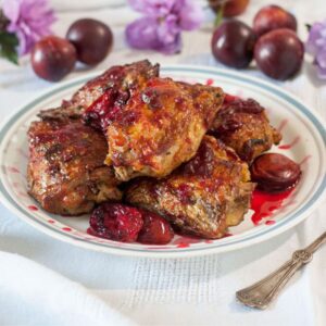 Chicken and plums piled on a white plate with a blue rim and drizzled with sauce.