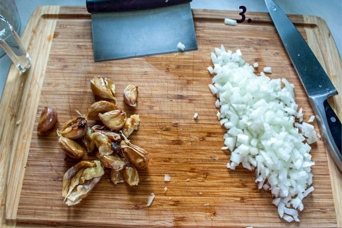 Choppped onion on a cutting borad next to roasted garlic cloves.