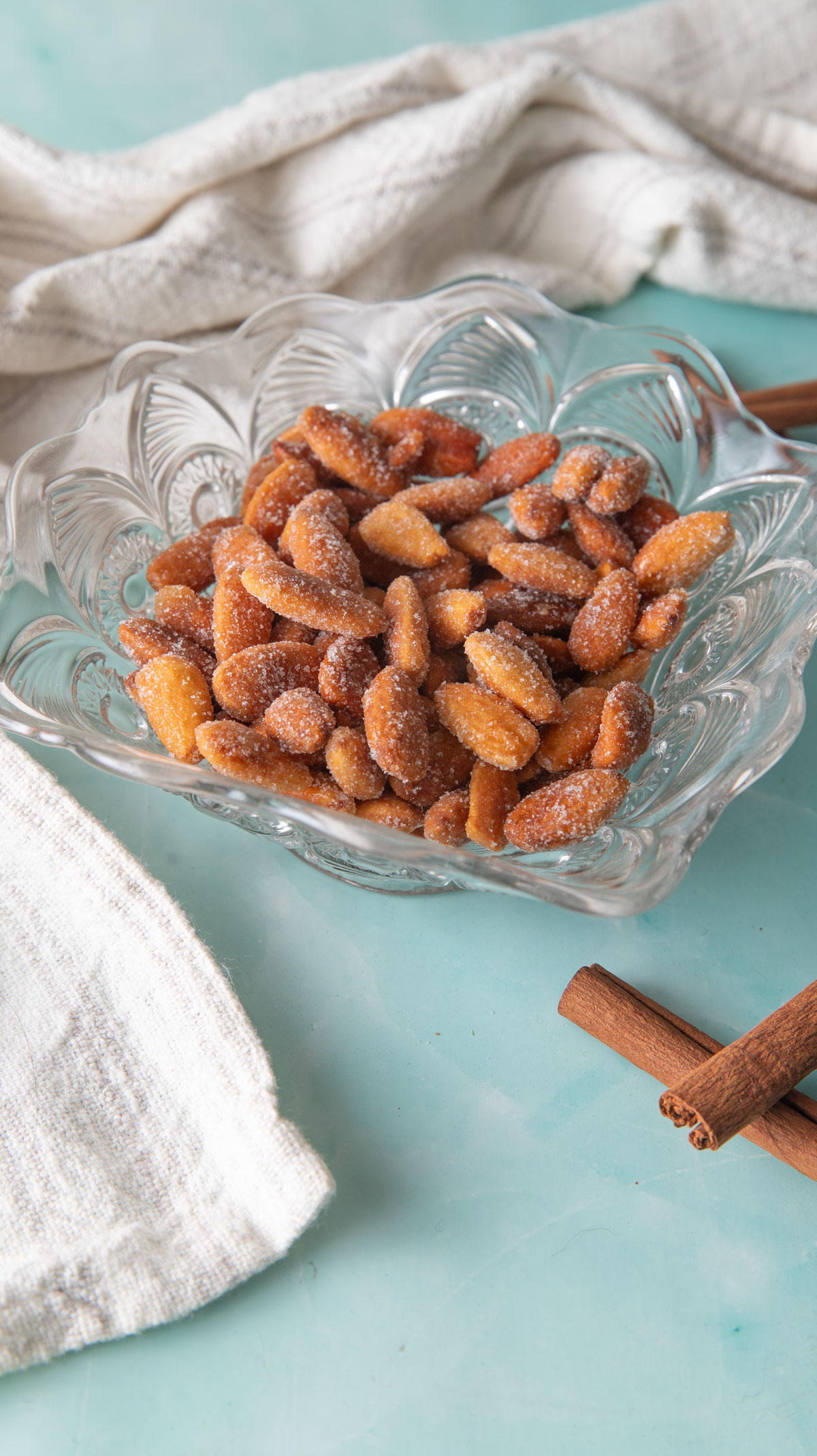 Honey-roasted almonds in a glass dish on a green background.