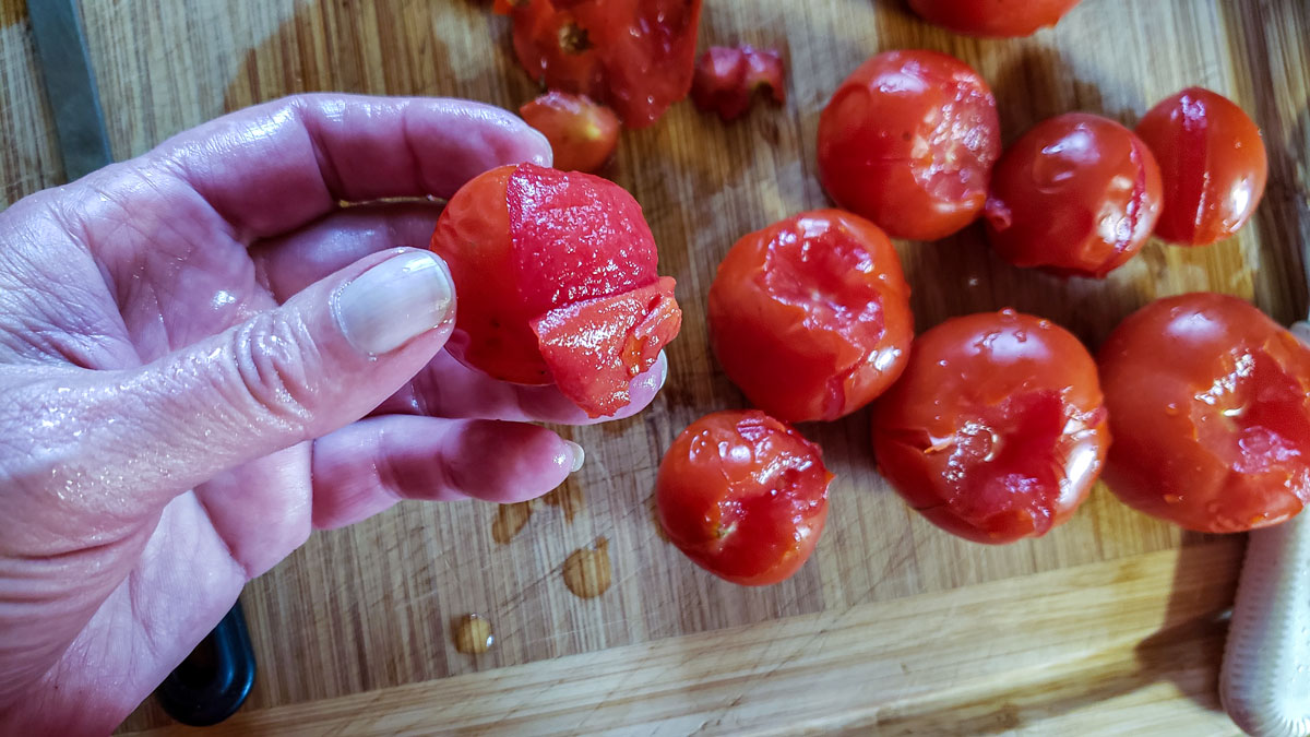 Woman's hand holding a tomato and peeling off the skin.
