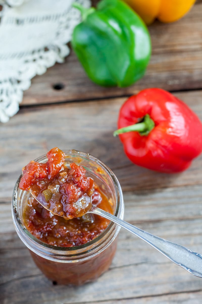 Open jar of Oscar Relish on antique barn wood table with colorful peppers.