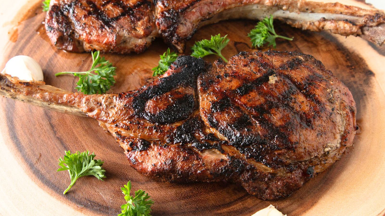 Two pork tomahawk chop on a wooden slab.