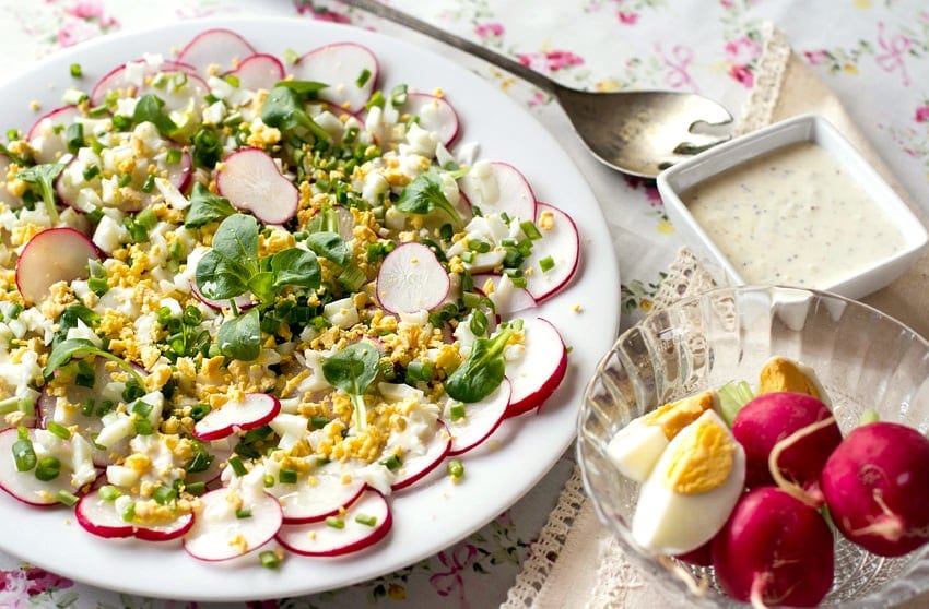 Bright Radish salad on a white plate with crumbled hard boiled eggs and shoots.