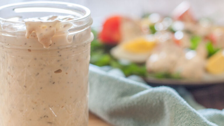 Jar with dripping thousand island dressing with a salad in the background.