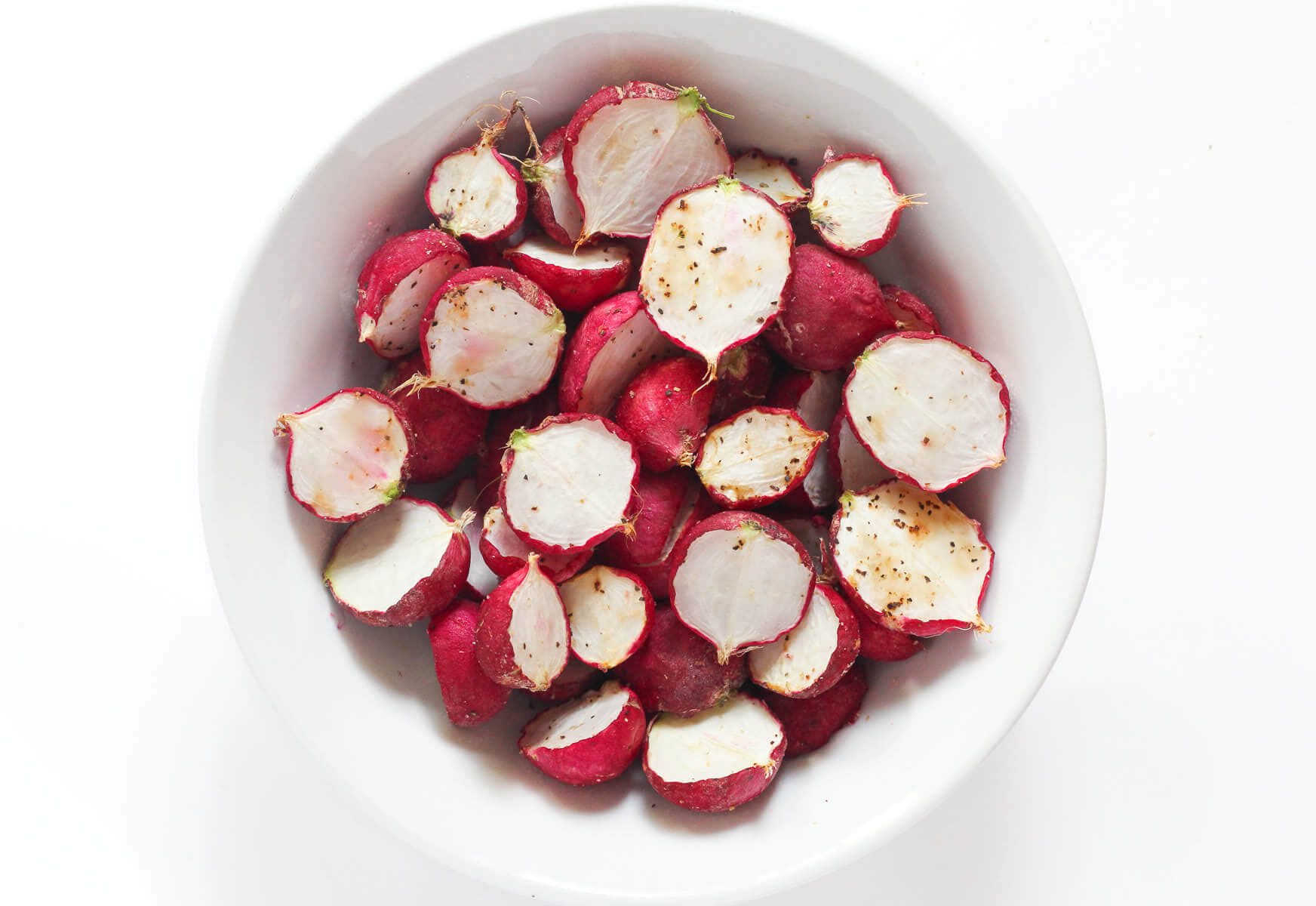 Roasted radishes in a white bowl on a white background.