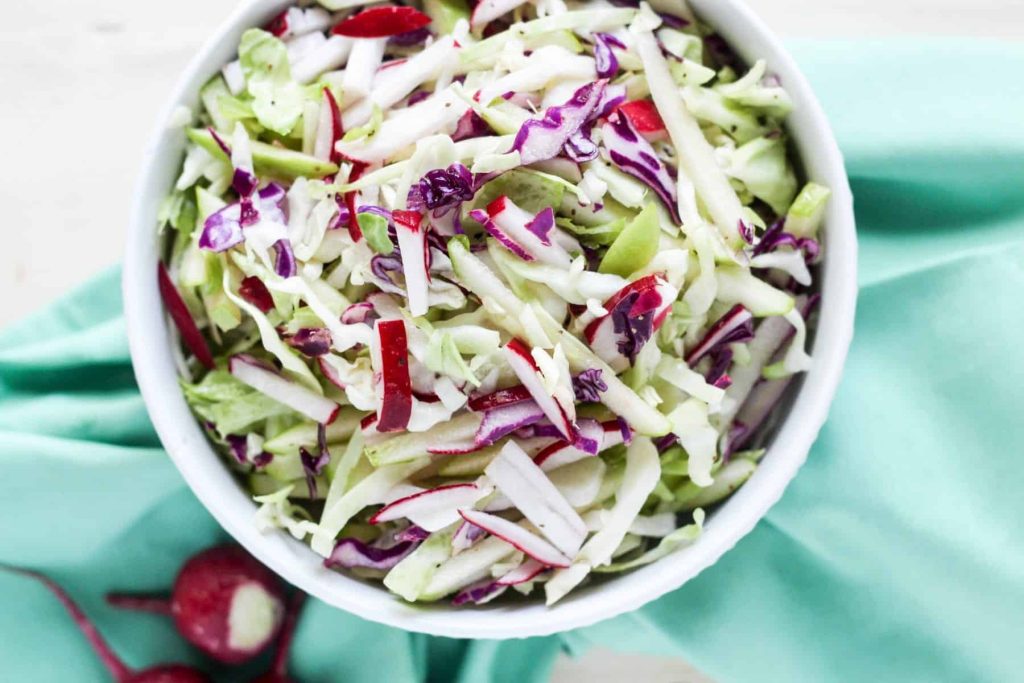 Cabbage apple and radish slaw in a white bowl on a green kitchen towel.