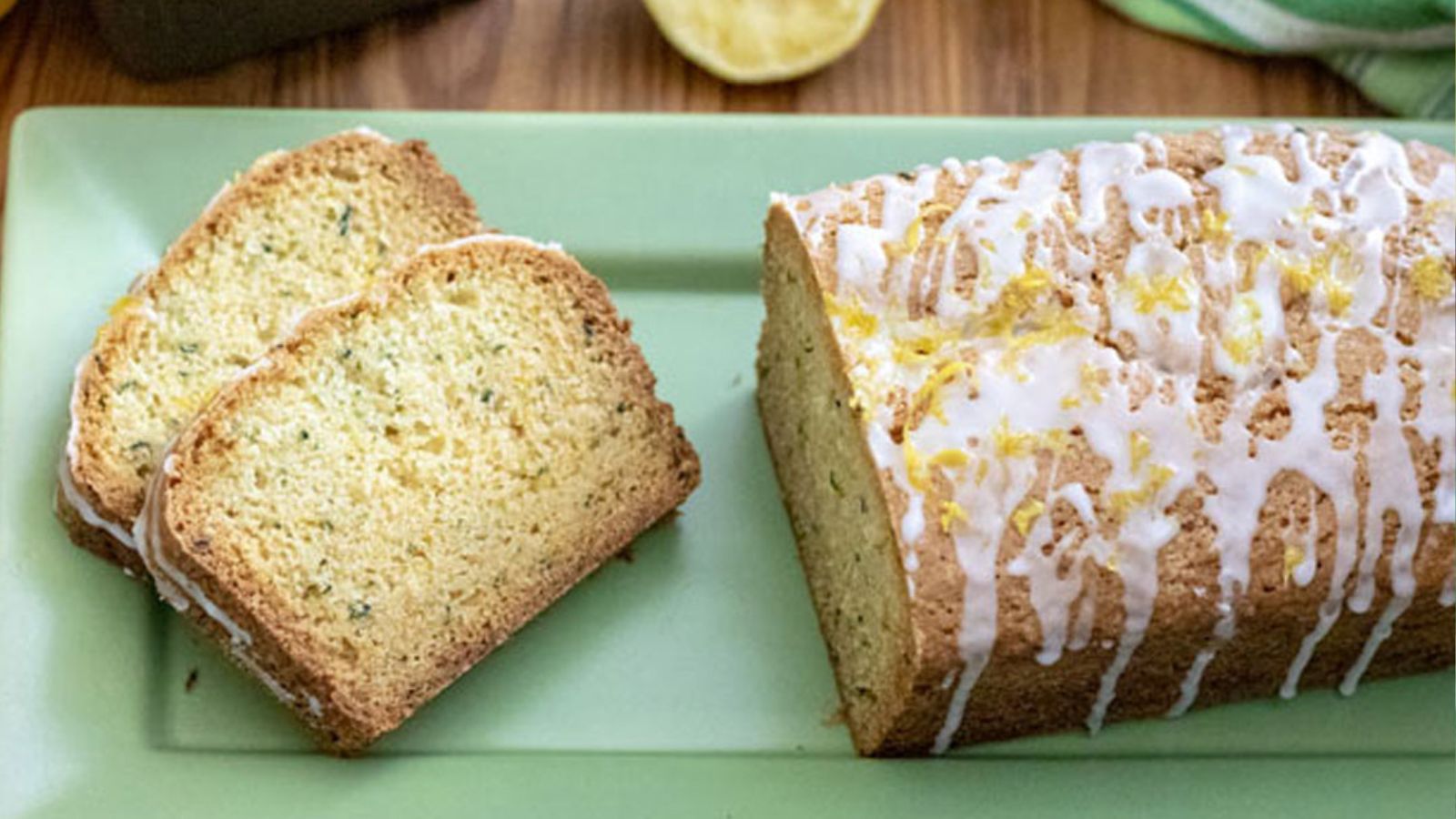 Two slices of lemon zucchini bread with the loaf on a green tray.