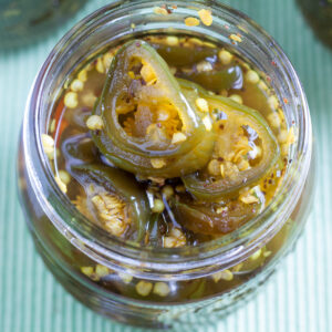 Closeup of opened jar of candied jalapeños, showing sliced peppers.