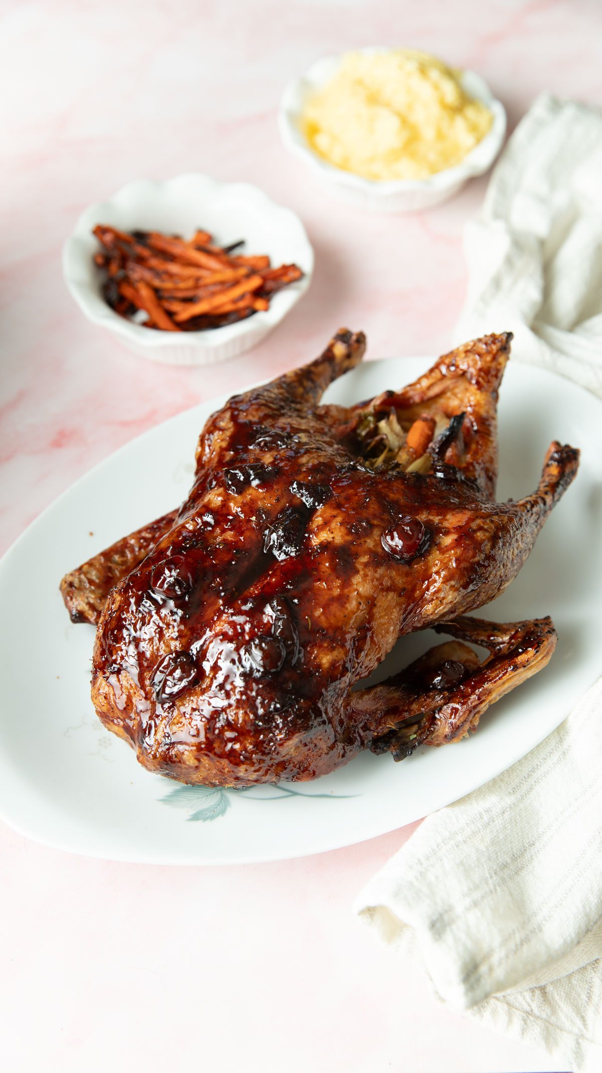 Cherry glazed duck on a white platter with side dishes on a pink background.