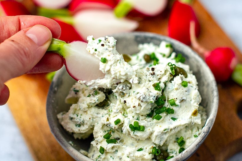 Woman's hand dipping a quartered radish into cream cheese dip.