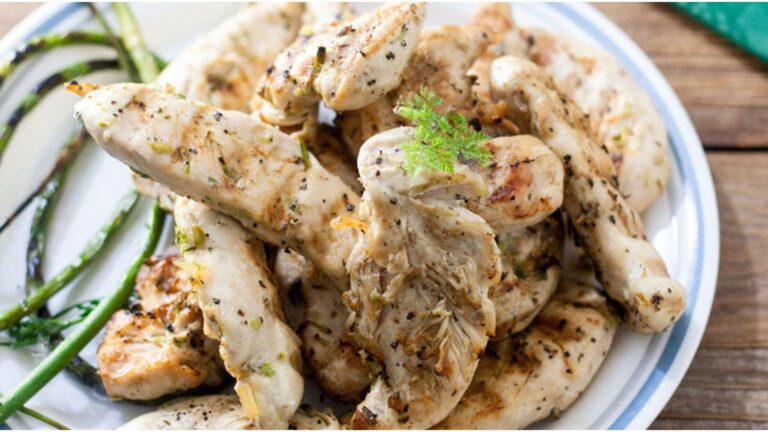 Chicken tenders piled on a plate with grilled garlic scapes.