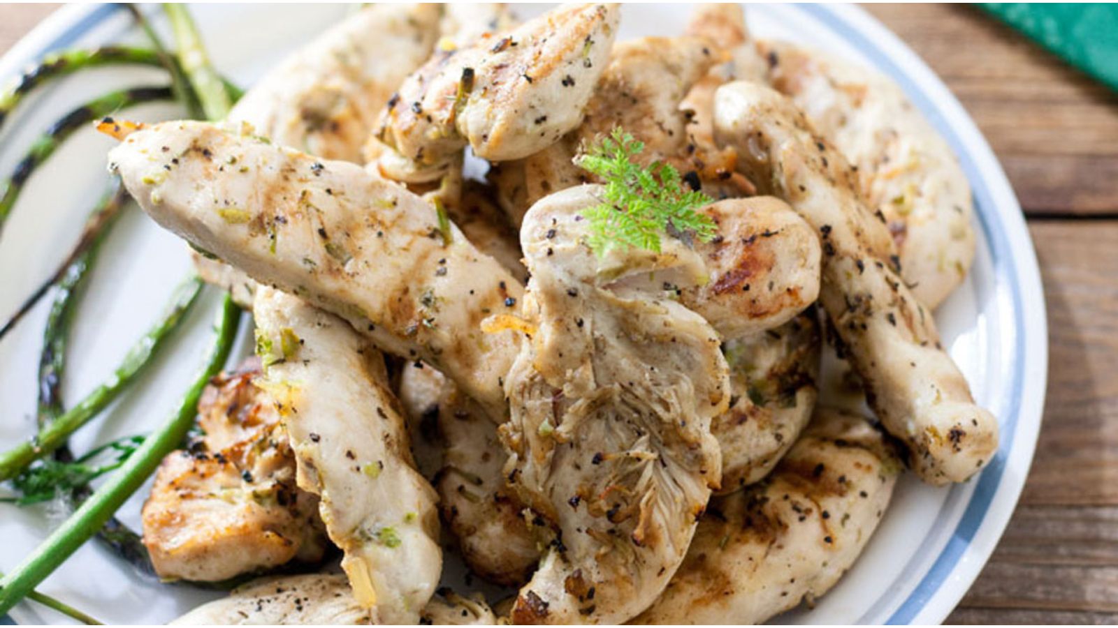 Chicken tenders piled on a plate with grilled garlic scapes.