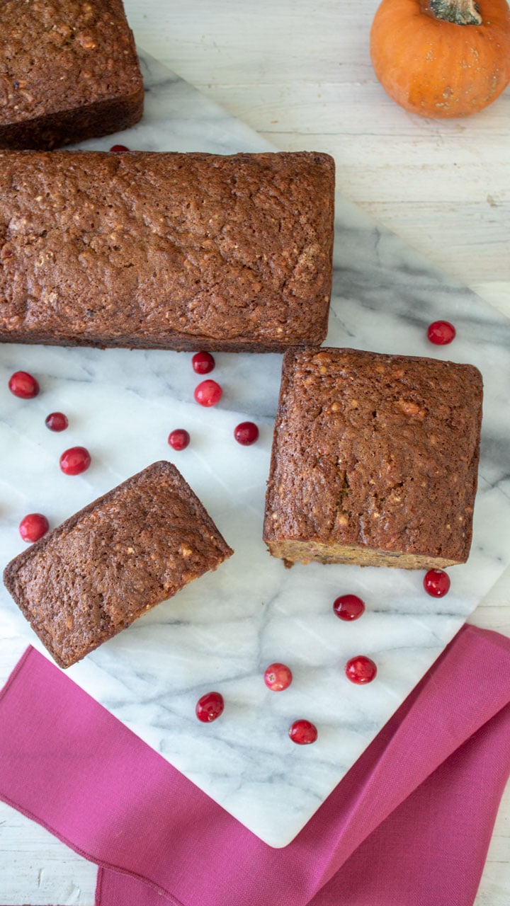 Whole cranberry pumpkin quick bread on marble board.