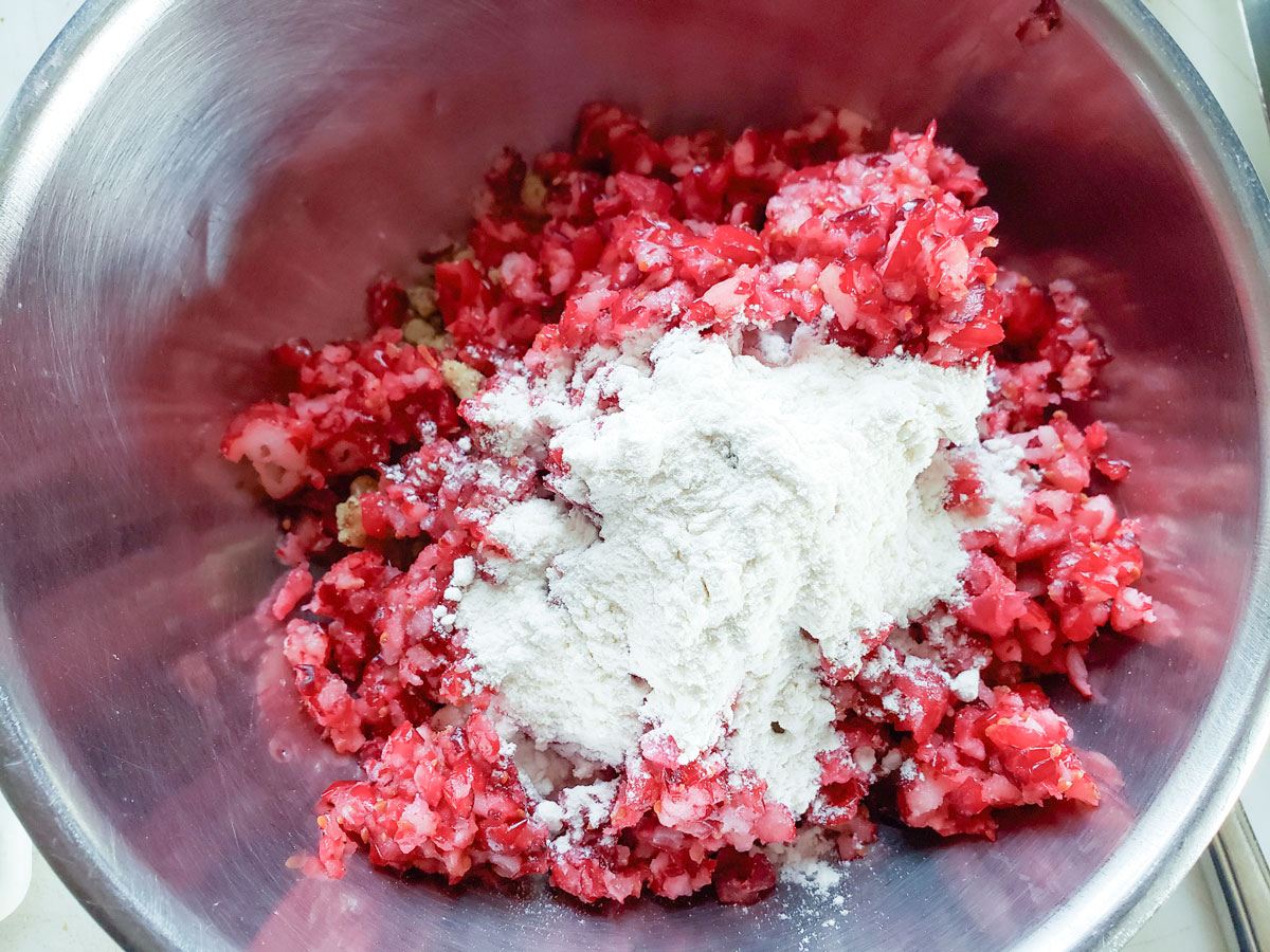 Flour added to the cranberries and nuts in the bowl.